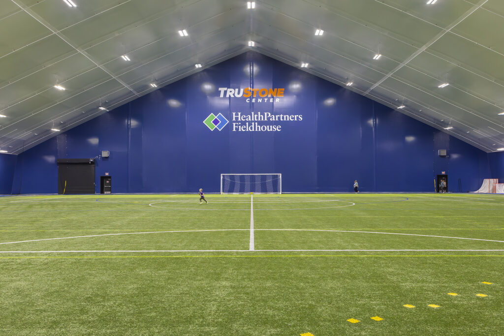 A young boy running across the field at an indoor fieldhouse